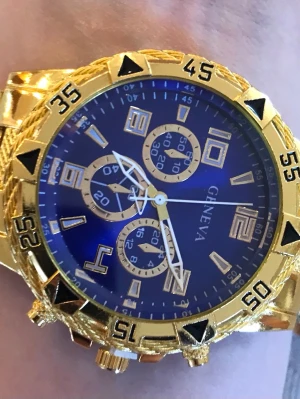 Guld- och blå klocka från Geneva - Stilren klocka från Geneva med blå urtavla och detaljer i guld. Klockan har flera små urtavlor, markerade siffror och en bred guldfärgad länk. Perfekt accessoar för dig som gillar att sticka ut med en lyxig look.