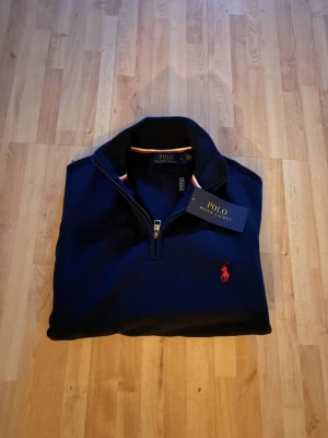 Ralph lauren quarterzip (M) Ny-oanvänd  - Säljer en helt ny och oanvänd Ralph Lauren quarter zip i stilren mörkblå färg. Klassisk och tidlös design med dragkedja i halsen och diskret broderad Ralph Lauren-logga på bröstet. Tröjan är tillverkad i hög kvalitet med mjukt och bekvämt material – perfekt för både vardag och mer uppklädda tillfällen. 🔹 Märke: Ralph Lauren 🔹 Modell: Quarter zip 🔹 Färg: Mörkblå 🔹 Skick: Helt ny / oanvänd 🔹 Passform: Klassisk Nypris är högt – perfekt möjlighet att göra ett fynd. Hör gärna av dig vid frågor eller 