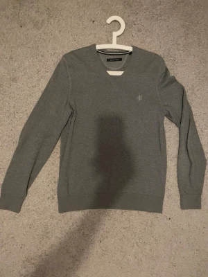 Grå stickad tröja Marc O'Polo - Snygg grå stickad tröja från Marc O'Polo med V-ringning och diskret logga broderad på bröstet. Tröjan har sngga ärmar och ribbade muddar vid ärmslut och nederkant. Perfekt till lager på lager och enkel att matcha med en vit tshirt. Pris ej hugget i sten. Skriv om frågor !