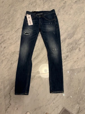 Helt nya donup - Säljer ett par mörkblå jeans från Dondup med snygga slitningar och lätt tvättade detaljer. Modellen är George! Klassisk femficksmodell med raka ben. Perfekta för dig som gillar en avslappnad och trendig look.