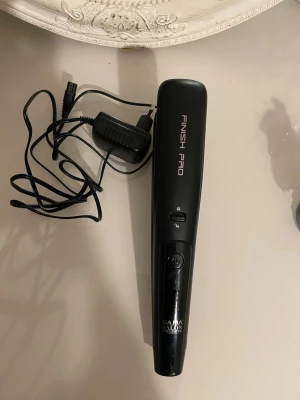 Finish Pro plattång svart - Finish Pro är en hårklippare som är utformad för att endast ta bort problematiska toppar samtidigt som hårets naturliga längd bibehålls. Den har en klipphöjd på 5 mm och en speciell design för behandling av skadade och kluvna toppar. Den skapar ett hälsosamt, välvårdat och snyggt utseende. Den fungerar med eller utan sladd i upp till 120 minuter utan laddning. Den levereras också med en speciell klippbehållare för att samla upp avklippt hår. Den fungerar antingen med nätström eller sladdlöst och