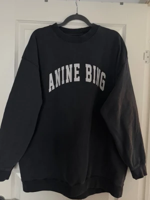 Mörkgrå sweatshirt från Anine Bing - Cool svart sweatshirt från Anine Bing med vit text framtill. Tillverkad i mjukt bomullsmaterial och har ribbade muddar vid ärmslut och nederkant. Perfekt för en avslappnad och trendig look. Använd fåtal gånger och i storlek M. Helt nytt skick 