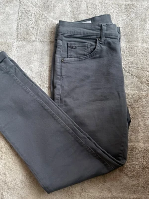 Grå slim fit jeans - Snygga mörkgrå jeans i slim fit-modell med klassisk femficksdesign och bälteshällor. Jeansen har en diskret logga på myntfickan och är tillverkade i ett mjukt, stretchigt material som ger skön passform.