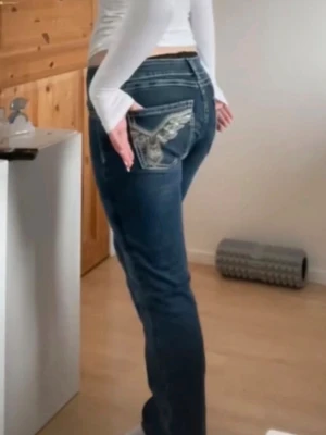 Blå bootcut jeans med broderade fickor - Säljer ett par blå bootcut jeans med snygga broderade detaljer på bakfickorna. Jeansen har normal midja, klassisk femficksmodell och är tillverkade i denim med lätt stretch. Perfekta för dig som vill ha en cool och avslappnad stil.