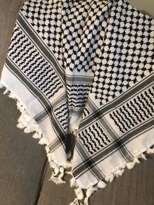 Palestina keffya Svartvit palestinasjal med tofsar ny förpackning  - Säljer en klassisk svartvit palestinasjal med traditionellt mönster och vita tofsar längs kanterna. Sval och mjuk, perfekt att styla runt halsen eller över axlarna. Materialet känns som bomull.