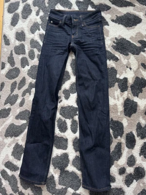 Mörkblåa jeans från Weekday - Snygga väldigt mörkblåa jeans från Weekday, i en mer straight/skinny modell med väldigt låg midja. Jeansen har storlek W23/L30, längden har varit perfekt på mig som är ca 162 cm☺️ Säljer då de är för små på mig. Väldigt sparsamt använda men som man ser på bild 5 har lappen på baksidan börjar släppa, annars inga defekter på dom!