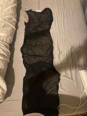 Svart meshklänning med omlott - Säljer en svart, tight meshklänning med omlottdetaljer och ärmlös design. Klänningen har en kroppsnära passform och transparenta partier som ger en edgy look. Perfekt för dig som vill sticka ut och gillar trendiga plagg.