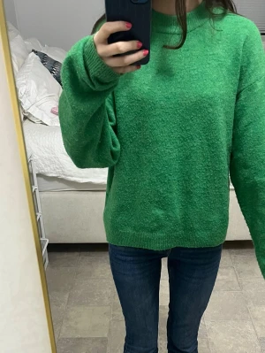Grön stickad tröja från H&M - Säljer en grön stickad tröja från H&M i storlek XS. Tröjan har en avslappnad passform, rund halsringning och ribbade muddar vid ärmslut och nederkant. Perfekt för lager på lager och enkel att styla med jeans eller kjol.
