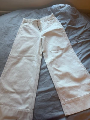 Vita vida jeans från H&M - Säljer ett par vita jeans från H&M med breda ben och hög midja. Klassisk femficksmodell med knappgylf och bälteshällor. Perfekta för en trendig och avslappnad look. Materialet är kraftigt denim i bomull.