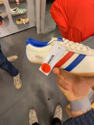 Adidas Tokyo sneakers retrostil - Snygga Adidas Tokyo sneakers i retrostil med vit ovandel, blå och röd rand på sidan samt blå häl och innerfoder. Klassisk gummisula och låg profil. Perfekta för dig som gillar vintagevibbar och sportig look.