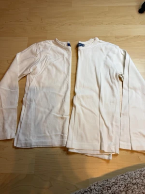 Vita långärmade tröjor Comp KappAhl - Två vita långärmade tröjor från Comp by KappAhl i storlek 134/140. Klassisk rak modell med rund halsringning, perfekta som basplagg. Tillverkade i mjukt och stretchigt material för skön passform.
