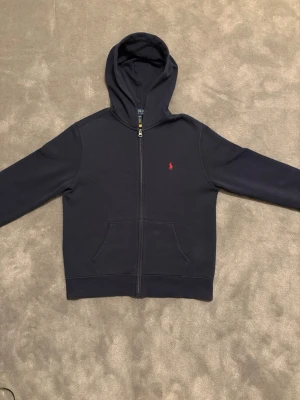 Polo Ralph Lauren hoodie - En mörkblå zip hoodie från Polo Ralph Lauren. Inga skavanker eller andra problem. Mycket gott skick. Mjuk skön bomull inuti. Nypris ligger på ca 1200kr