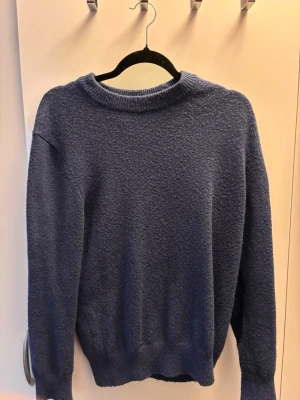 Mörkblå stickad tröja från H&M - Mysig mörkblå stickad tröja från H&M med rund halsringning och ribbade muddar vid ärmslut och nederkant. Tröjan har en enkel, klassisk design och är perfekt för lager på lager under kyliga dagar.