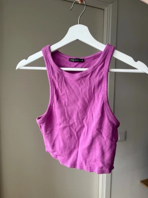 Ribbad lila topp Zara - Trendig ribbad croppad linnetopp från Zara i en snygg lila/rosa färg. Toppen har breda axelband och rund halsringning, perfekt för att styla med höga jeans eller kjol. Materialet är mjukt och stretchigt för en bekväm passform. Storlek L men passar S-M.
