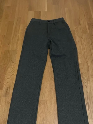 Mörkgrå kostymbyxor med raka ben - Snygga mörkgrå kostymbyxor med klassisk rak passform och bälteshällor. Byxorna har diskreta fickor bak och framtill, samt stängs med knapp och dragkedja. Perfekta för en clean och stilren look.