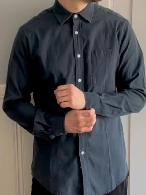 Mörkblå skjorta från Newboat - Stilren mörkblå skjorta från Newboat i regular fit. Skjortan har klassisk krage, vita knappar framtill och lång ärm. Tillverkad i mjuk bomull som känns skön mot huden. Perfekt för dig som gillar enkel och clean stil.