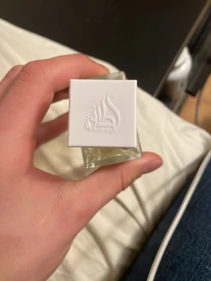 Lattafa Eau de Parfum 60ml - Lattafa Eau de Parfum i en stilren, transparent glasflaska med vit fyrkantig kork och silverdetaljer. Flaskan rymmer 60 ml och har en modern design med logotyp på korken. Perfekt för dig som vill ha en unik och elegant parfym. Den är inspirerad av erba pura. Den är helt ny och inte använd 