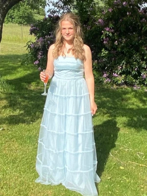 Ljusblå långklänning med volanger - Säljer en ljusblå axelbandslös långklänning med flera lager volanger. Klänningen har en romantisk och flowy känsla, perfekt för speciella tillfällen. Tillverkad i ett tunt, lätt material som ger ett drömmigt intryck. Den är änvänd en gång och är i mycket fint skick. Storlek UK 12, men liten i storleken så skulle säga storlek S-M för det är den storleken jag har.                                                             Nypris 1700kr, tänkt pris 700kr
