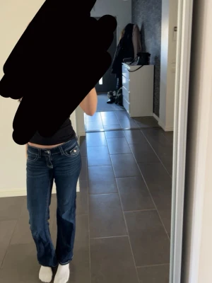 Mörkblå bootcut jeans med kontrastsömmar - Säljer ett par mörkblå bootcut jeans med vita kontrastsömmar och snygga fickdetaljer bak med lock och knapp. Jeansen har låg midja och klassisk femficksdesign. Perfekta för en avslappnad och trendig look. Low waisted jeans som passar till allt! Säljs för att den är för små❣️