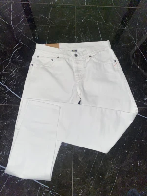 Vita jeans från dondup - Säljer ett par snygga vita jeans från Dondup med klassisk femficksmodell och raka ben. Jeansen har silverfärgade nitar och en liten logga på bakfickan. Perfekta för dig som vill sticka ut med en clean och fräsch look.