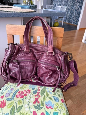 Plommonfärgad väska från Zadig & Voltaire - Säljer en så fin vinröd handväska från Zadig & Voltaire som är väldigt rymlig! Den är i mjukt skinn och har flera dragkedjefickor framtill och justerbar axelrem. Den har dubbla handtag och detaljer i silverfärgad metall. Perfekt för dig som vill sticka ut lite, skriv vid frågor😊