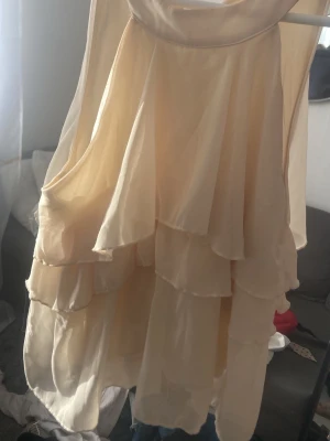 Champagnefärgad volangklänning - Säljer en champagnefärgad kortklänning med flera lager volanger och ärmlös design. Klänningen har en mjuk, flytande form och är tillverkad i ett tunt, lätt material som ger ett romantiskt intryck. Perfekt för sommarens alla tillfällen!