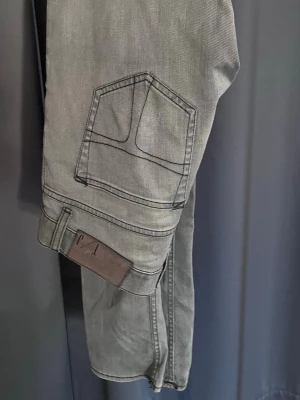 Tiger of Sweden Jeans - Säljer ett par grå jeans från Tiger of Sweden med raka ben och klassisk femficksdesign. Jeansen har en snygg tvättad look och detaljerade sömmar på bakfickorna. Tillverkade i mjukt denimtyg som ger en skön passform. W31 L32