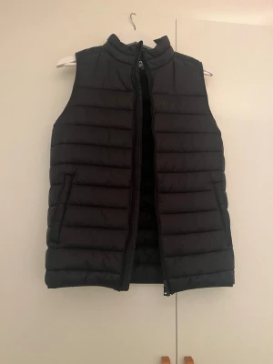 Everest svart lättviktsväst – storlek 170/176 - Svart lättviktsväst från Everest modell. Storlek 170/176 (passar tonåring eller mindre vuxen beroende på passform). Den är i bra skick. Skicka bara meddelande ifall ni undrar något mer