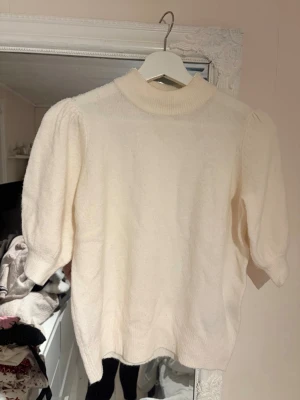 Vit stickad tröja med puffärm - Säljer en krämvit stickad tröja med puffärmar och ribbad hög hals. Tröjan har en mjuk och mysig känsla, samt halvlånga ärmar som ger en trendig siluett. Perfekt att styla med jeans eller kjol för en clean look. Storlek m men passar s också