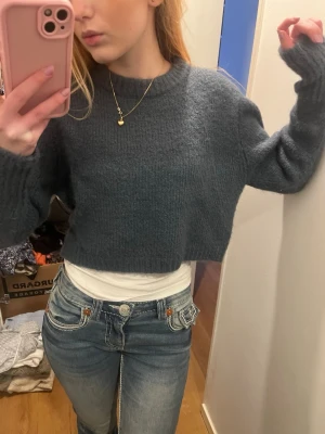 Grön/blå cropped stickad tröja Zara - Säljer en mörkgrå cropped stickad tröja från Zara. Tröjan har en avslappnad passform, ribbade muddar och rund halsringning. Perfekt att styla med höga jeans för en trendig look.