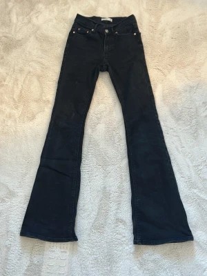 Svarta bootcut jeans med utsvängda ben - Säljer ett par svarta bootcut jeans med hög midja och utsvängda ben. Klassisk femficksmodell med knapp- och dragkedjestängning. Snygga att styla med sneakers eller boots för en trendig look.