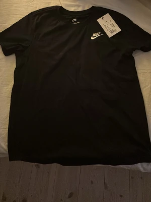 Svart Nike t-shirt med logga - Klassisk svart t-shirt från Nike med vit broderad logga på bröstet. T-shirten har rund halsringning och korta ärmar. Tillverkad i mjuk bomull för en skön och avslappnad stil. Perfekt till jeans eller shorts. Prislapp fortfarande på!