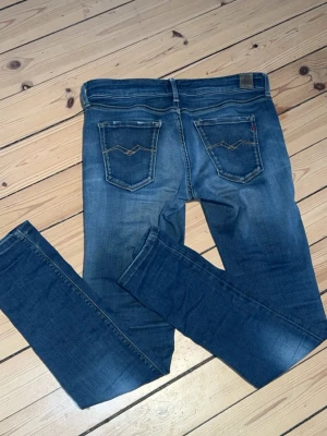 Blå slim fit jeans från Replay  - Snygga blå slim fit jeans från Replay med klassiska bakfickor och gul kontrastsöm. Jeansen har en tvättad look med slitningar och är tillverkade i denim. Perfekta för en avslappnad och trendig stil.