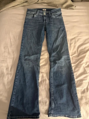 Blå bootcut jeans med broderade fickor - Säljer ett par blå bootcut jeans med snygga broderade detaljer på bakfickorna. Köpte för 699kr för inte så länge sen så ganska nya .Jeansen har klassisk femficksmodell, låg midja och är tillverkade i denim med lätt tvättad look. Perfekta för dig som gillar retrostil och vill ha ett par jeans med schysst passform.