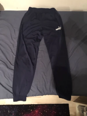 Svarta mjukisbyxor från Puma - Säljer ett par svarta mjukisbyxor från Puma med resår i midjan och vid bensluten. Byxorna har en klassisk rak passform och Puma-loggan i vitt på vänster lår. Perfekta för chill eller träning.