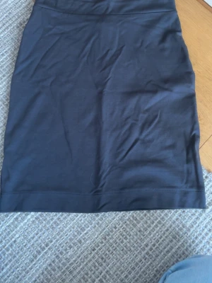 Svart kortkjol i bomull - En enkel och stilren svart kortkjol i mjukt bomullsmaterial. Kjolen har en rak och tajt passform och är perfekt för att matcha med olika toppar. Inga synliga detaljer eller mönster, vilket gör den lätt att styla.