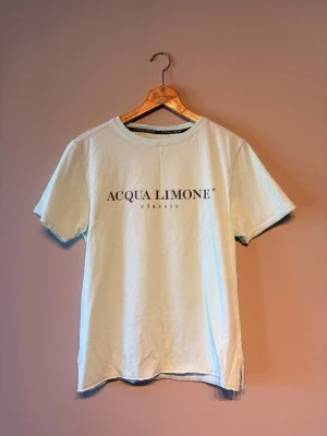 Ljusblå Acqua Limone t-shirt - Snygg ljusblå t-shirt från Acqua Limone med klassisk logga framtill och en stor gul citron-grafik på ryggen. T-shirten har rund hals och korta ärmar, perfekt för en avslappnad stil. Tillverkad i mjuk bomull för skön komfort.