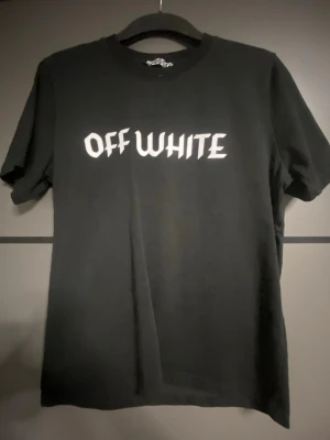 Svart Off-White t-shirt med tryck - Snygg svart t-shirt från Off-White med vit logga framtill och stort tryck av Bugs Bunny i blått och vitt på ryggen. Klassisk rund hals och korta ärmar. Perfekt för dig som gillar streetwear och vill sticka ut med en unik design.