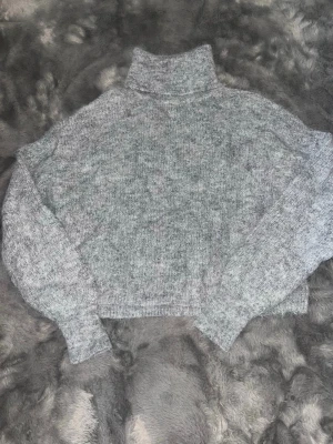 Gråmelerad stickad polotröja - Mysig gråmelerad stickad polotröja med lös passform och långa ärmar. Tröjan har en hög polokrage, Perfekt för kyliga dagar och enkel att matcha med olika outfits.