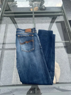Nudie Jeans Bootcut Eddy – Dark Superblue (W33/L34) - Säljer ett par riktigt snygga Nudie Jeans i modellen "Bootcut Eddy". Färgen är "Dark Superblue", en tidlös mörkblå tvätt som funkar till allt. Jeansen har 2% elastan i tyget, vilket gör att de sitter riktigt bra och är sköna att bära hela dagen. En klassisk modell med bra kvalitet som håller länge.  Modell: Bootcut Eddy.  Storlek: W33 L34.  Material: 98% bomull, 2% elastan (skön stretch).  Skick: Mycket fint skick. Hör av dig om du har några frågor eller vill se fler bilder! 