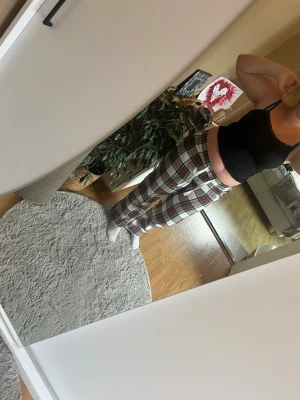 Rutiga loungewear-byxor med dragsko - Säljer ett par mysiga loungewear-byxor med klassiskt rutigt mönster i vitt, rött, grönt och svart. Byxorna har resår i midjan och vit dragsko för skön passform. Perfekta för chill hemma eller slappa dagar.