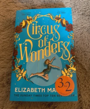 Circus of Wonders av Elizabeth Macneal - En färgstark roman med blått omslag och guldiga detaljer. Omslaget pryds av cirkusinspirerad grafik och en akrobat. Boken är på engelska och handlar om Nell som blir stjärna i ett cirkussällskap i 1800-talets England. Perfekt för dig som gillar historisk och fantasifull skönlitteratur.