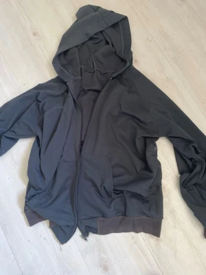 Mörkgrå hoodie med dragkedja - Snygg mörkgrå hoodie med dragkedja framtill och stor huva. Tröjan har två fickor på magen och ribbade muddar vid ärmslut och nederkant. Perfekt för en avslappnad och chill stil.