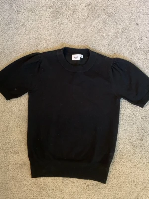 Svart topp med puffärm från Saint - En svart topp från Saint med puffiga korta ärmar och rund halsringning. Materialet är mjukt och stretchigt, perfekt för en stilren look. Enkel men ändå trendig design som passar till mycket.
