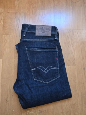 Mörkblå jeans från Replay - Snygga mörkblå jeans från Replay med klassisk femficksdesign och kontrastsömmar. Jeansen har en rak passform och detaljerade bakfickor med broderi. Perfekta för en stilren och avslappnad look. W31 L32
