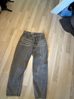 Grå jeans med hög midja - Säljer ett par grå jeans med hög midja och raka ben. Jeansen har klassisk femficksdesign, bälteshällor och är tillverkade i denim. Perfekta för en avslappnad och trendig look. 27 midjan i storlek och 30 längd 