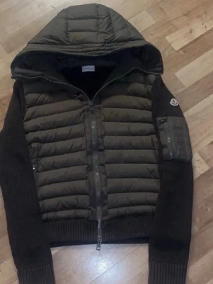 Mörkgrön Moncler cardigan  - Snygg mörkgrön pufferjacka med stickade ärmar och quiltad kropp. Jackan har huva, dragkedja framtill och en ficka med dragkedja på ärmen. Perfekt för kyligare dagar och har en modern, sportig look.Jätte bra skick 