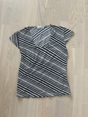 Randig svartvit v-ringad topp - Snygg topp med svartvita diagonala ränder och v-ringning. Kortärmad och figurnära passform, perfekt till jeans eller kjol. Tillverkad i mjukt material som känns skönt mot huden. Stretchig så passar M/L även men storlek S passar super på mig som vanligtvis är S! 