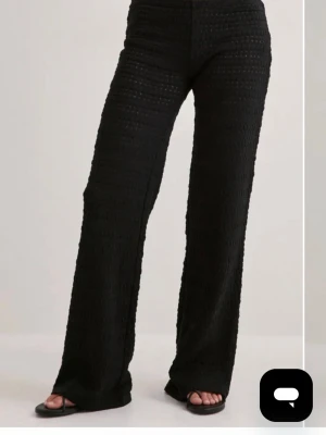 Svarta vida virkade byxor  - Snygga svarta leggings med virkad struktur och utsvängda ben. Hög midja och genombrutet mönster ger en trendig look. Perfekta att styla med crop tops eller oversized skjortor för en cool vibe.