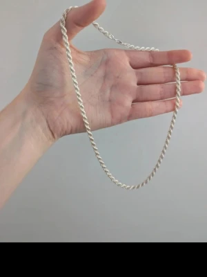 Tjockt silverfärgat kedjehalsband - Säljer ett stilrent halsband i silverfärg med tvinnad kedja. Halsbandet har en enkel och klassisk design som passar till många olika stilar. Materialet ser ut att vara metall och längden är ungefär 45 cm. Perfekt för dig som gillar minimalistiska accessoarer.